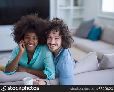 young multiethnic couple sitting on sofa at home drinking coffe, talking, smiling.