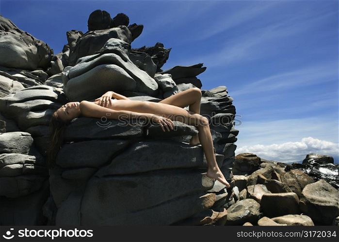 Young multiethnic woman sunbathing nude on rocks at Maui Hawaii beach.