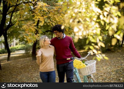 Young multiracial couple walking through park and  pushing a bicycle