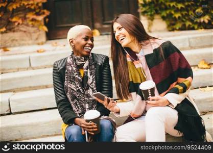 Young multiracial friends sitting in autumn park, talking and carry coffee to go in the hands