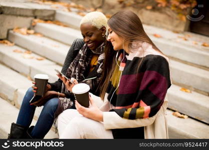 Young multiracial friends sitting in autumn park, talking and carry coffee to go in the hands