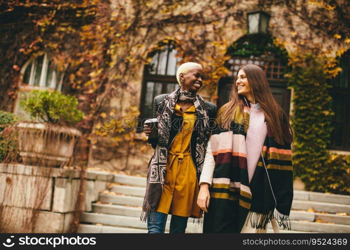 Young multiracial friends walking around autumn park, talking and carry coffee to go in the hands