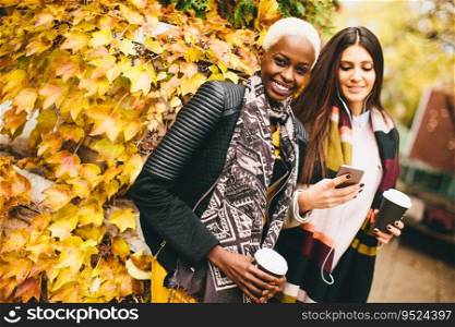 Young multiracial friends walking around autumn park, talking and carry coffee to go in the hands