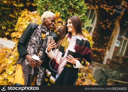 Young multiracial friends walking around autumn park, talking and carry coffee to go in the hands