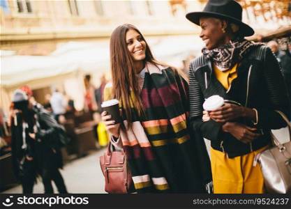 Young multiracial  friends walking around the town, talking and carry coffee to go in the hands