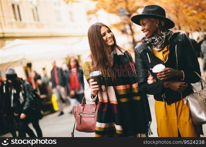 Young multiracial  friends walking around the town, talking and carry coffee to go in the hands