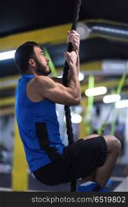 young muscular man doing rope climbing in cross fitness gym. man doing rope climbing