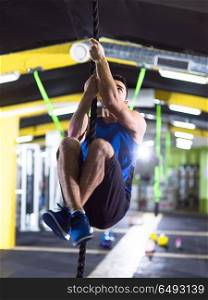 young muscular man doing rope climbing in crossfitness gym. man doing rope climbing