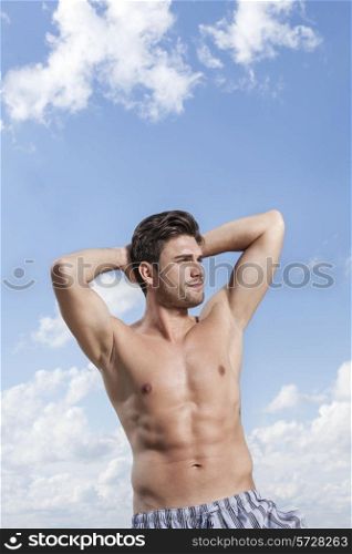 Young muscular man with hands behind head against cloudy sky