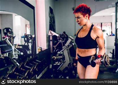 Young muscular strong woman holding dumbbells at the gym bodybuilding weight lifting fitness arm biceps training