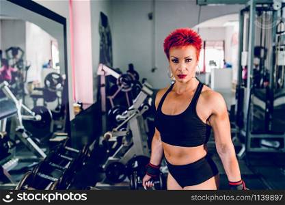 Young muscular strong woman holding dumbbells at the gym bodybuilding weight lifting fitness training