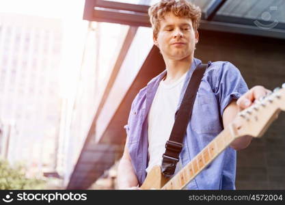 Young musician with guitar in city. Portrait of young musician with guitar in city