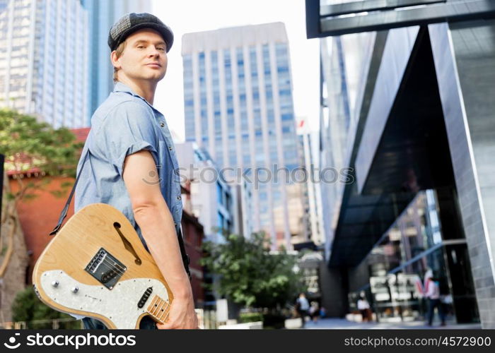 Young musician with guitar in city. Portrait of young musician with guitar in city