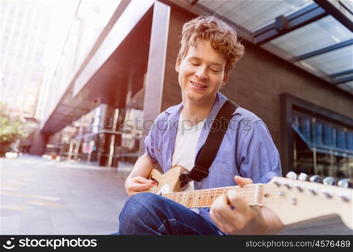 Young musician with guitar in city. Portrait of young musician with guitar in city