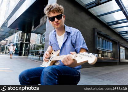 Young musician with guitar in city. Portrait of young musician with guitar in city