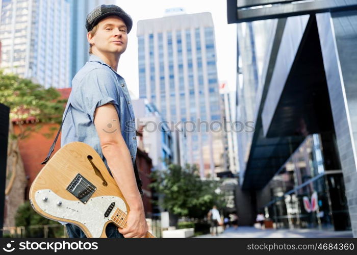 Young musician with guitar in city. Portrait of young musician with guitar in city