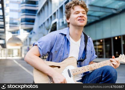 Young musician with guitar in city. Portrait of young musician with guitar in city