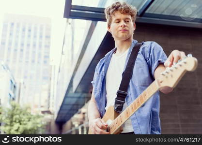 Young musician with guitar in city. Portrait of young musician with guitar in city