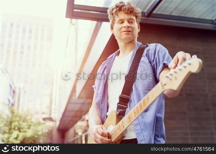 Young musician with guitar in city. Portrait of young musician with guitar in city