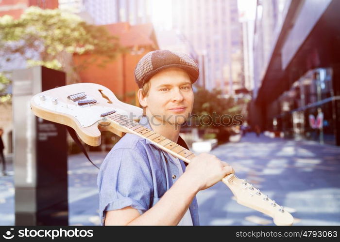 Young musician with guitar in city. Portrait of young musician with guitar in city