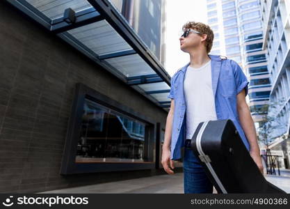 Young musician with guitar in city. Portrait of young musician with guitar in city