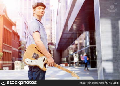 Young musician with guitar in city. Portrait of young musician with guitar in city