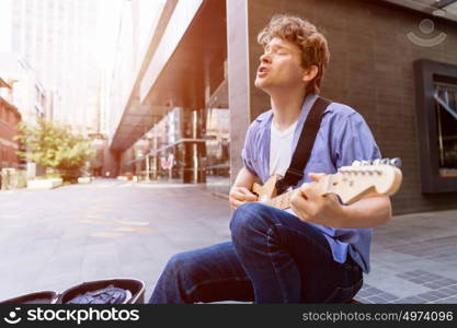 Young musician with guitar in city. Portrait of young musician with guitar in city