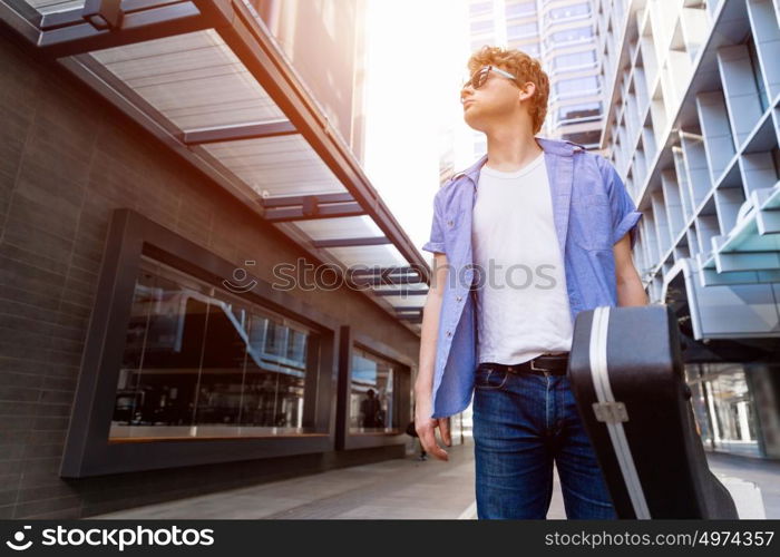 Young musician with guitar in city. Portrait of young musician with guitar in city