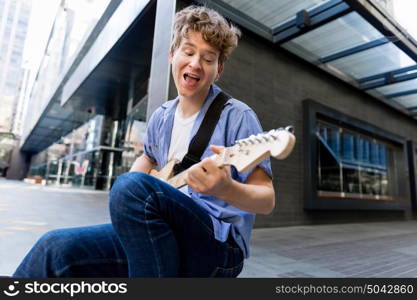 Young musician with guitar in city. Portrait of young musician with guitar in city