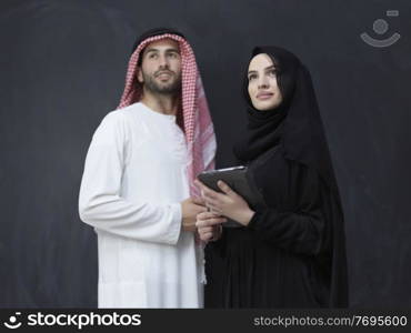 young muslim business couple arabian man with woman in fashionable hijab dress using mobile phone and tablet computer in front of black chalkboard representing modern islam fashion technology and ramadan kareem concept