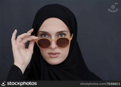 Young muslim in traditional clothes or abaya and sunglasses posing in front of black chalkboard. Arab woman representing modern arabic lifestyle, islamic fashion and Ramadan kareem concept