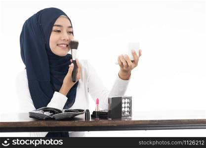 Young Muslim woman do face cosmetic with mirror and makeup brush on white background taken in studio. Using for Fashion and beauty concept