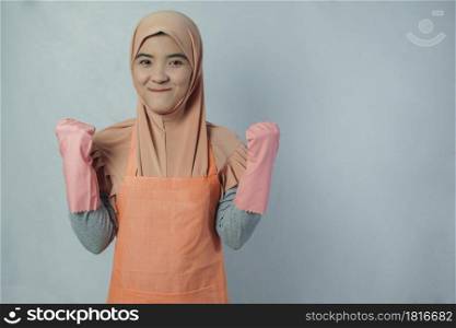 Young muslim woman housewife with pink rubber gloves in apron Hands clasped on both sides and ready to clean house on grey background