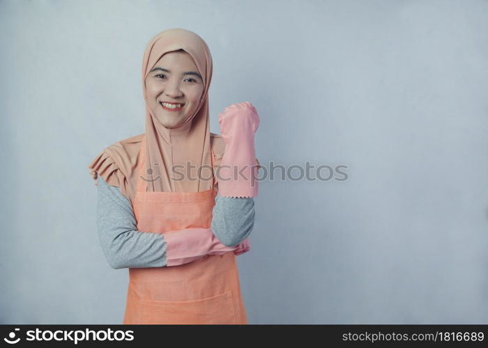 Young muslim woman housewife with pink rubber gloves in apron on grey background