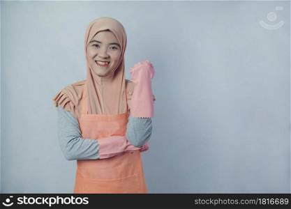 Young muslim woman housewife with pink rubber gloves in apron on grey background