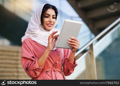 Young Muslim woman wearing hijab headscarf using digital tablet in business environment. Young Arab woman wearing hijab using digital tablet outdoors
