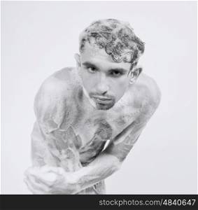 Young naked man taking a shower in the foam with a beautiful body on white background