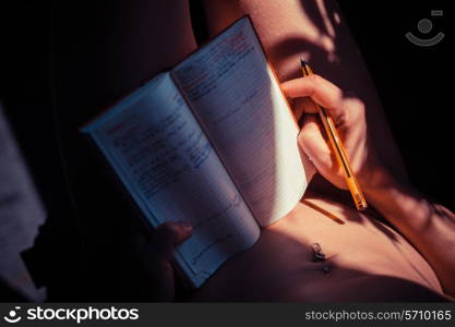 Young naked woman is writing in a notebook