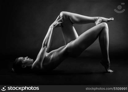 Young naked woman posing on black background. Perfect skin. Black and white photograph