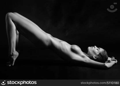Young naked woman posing on black background. Perfect skin. Black and white photograph