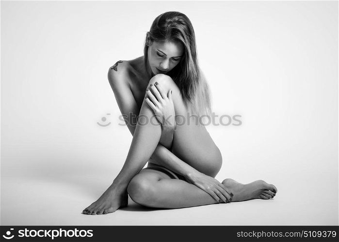 Young naked woman sitting on white floor. Perfect skin. Black and white photograph