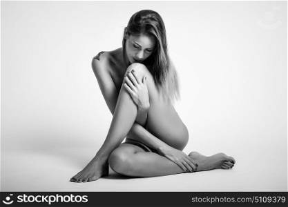 Young naked woman sitting on white floor. Perfect skin. Black and white photograph