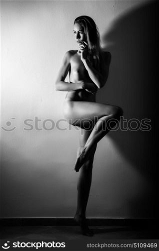 Young naked woman standing on white wall. Perfect skin. Black and white photograph