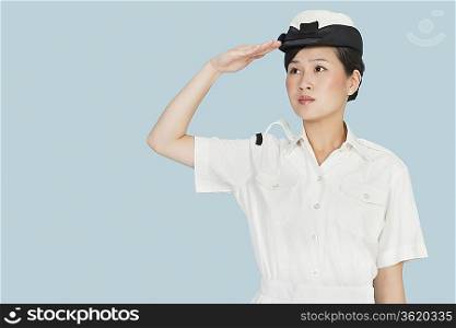 Young Navy officer looking away as she salutes against light blue background