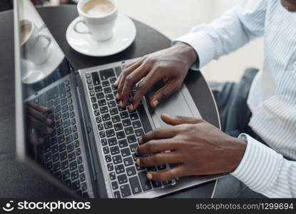 Young negro businessman working on laptop in car showroom. Successful business person on motor show, black man in formal wear. Businessman working on laptop in car showroom