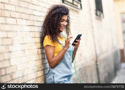Young North African woman texting with her smart phone outdoors. Smiling Arab girl in casual clothes with black curly hairstyle.. Young North African woman texting with her smart phone outdoors