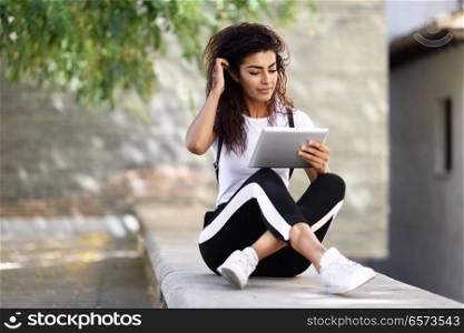 Young North African woman with looking at her digital tablet outdoors. Arab girl wearing sportswear urban background.