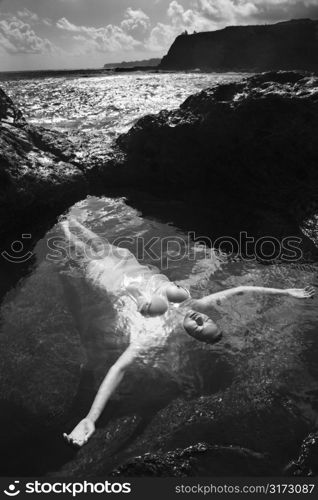 Young nude Asian woman floating in water with arms outstretched in Maui, Hawaii.