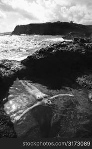 Young nude Asian woman floating in water with arms outstretched in Maui, Hawaii.