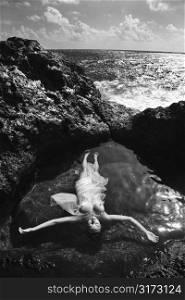 Young nude Asian woman floating in water with arms outstretched in Maui, Hawaii.